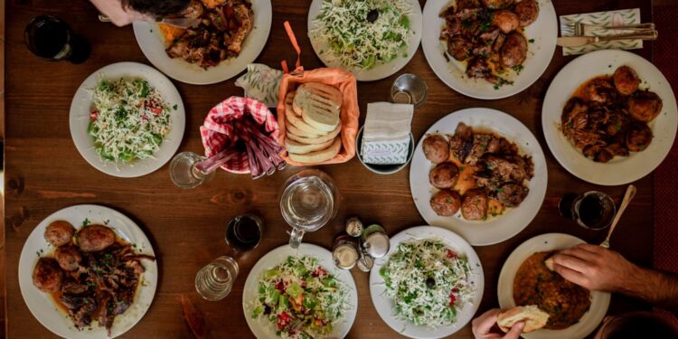A group of guests reaching across a communal table covered in shared dishes, celebrating the communal table tradition.