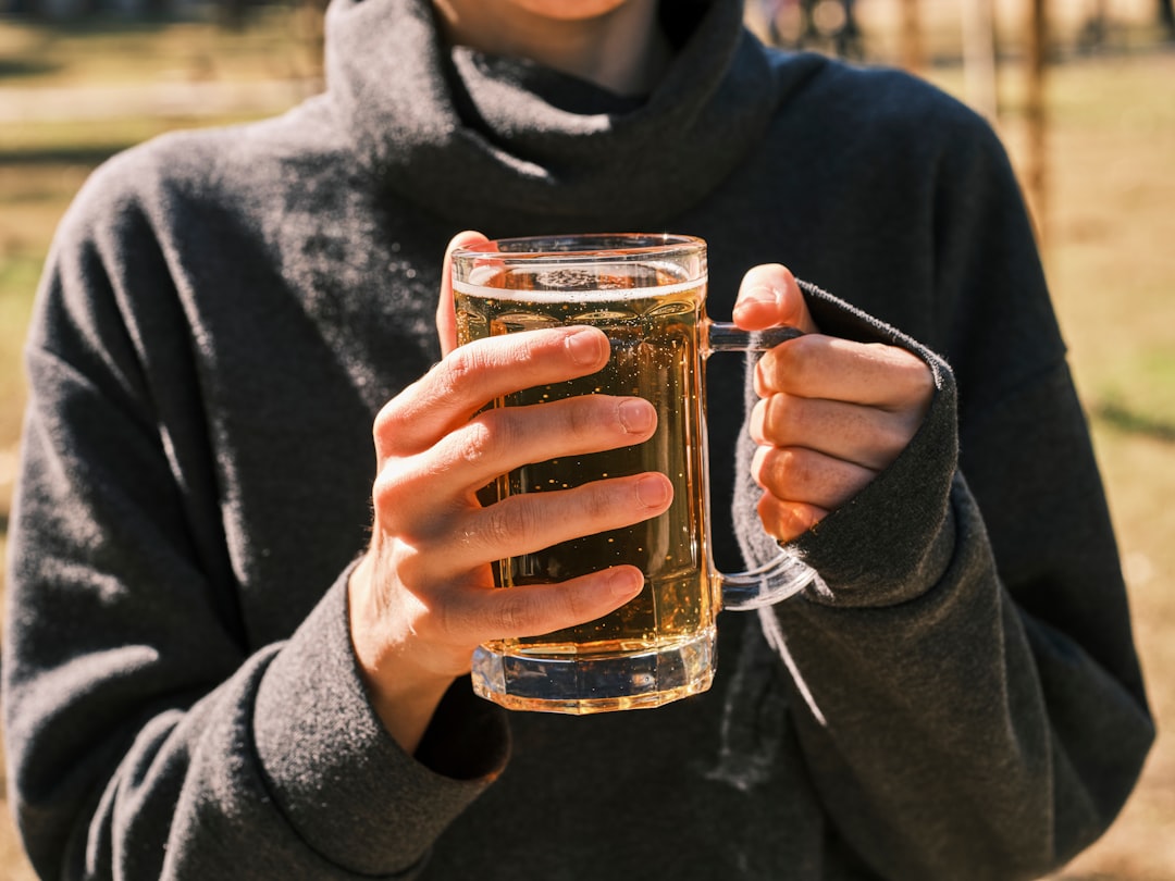 A person holding a glass of cold brew tea outdoors with sunlight filtering through the leaves in the background