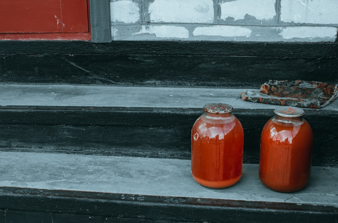 A cook carefully ladling a smooth, deeply coloured tomato sauce into glass storage jars.