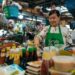 National Day dishes every table needs - GUSTOwebzine Vendor wearing a green GrabFood apron prepares sauces at a busy market stall with colorful bottles in the foreground.