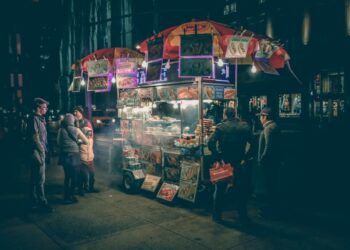 Nachtelijke streetfoodkar die oplicht met lichtjes terwijl klanten zich rond het menu verzamelen.
