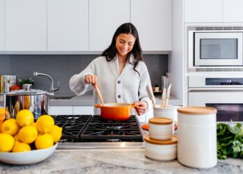 Een vrouw die een traditionele stoofpot bereidt in antieke aardenwerken potten boven een lage vlam in een rustieke keuken