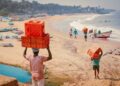 Coastal cuisine Indias most underrated seafood - GUSTOwebzine People carrying red plastic crates on a sandy beach with boats along the shore under a sunny sky.