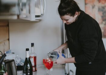 Een vrouw giet voorzichtig een glas gefermenteerde dranken in aan een lichte keukentafel, omgeven door seizoensgebonden herfstproducten
