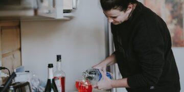 A woman carefully pouring a glass of fermented drinks at a bright kitchen counter, surrounded by seasonal autumn produce