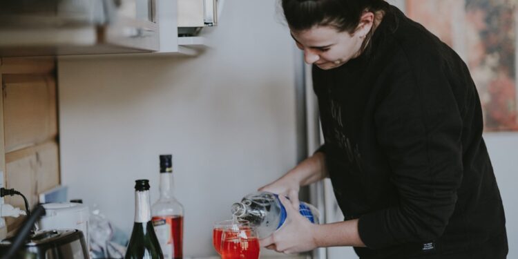 A woman carefully pouring a glass of fermented drinks at a bright kitchen counter, surrounded by seasonal autumn produce