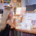 Gluten-free guide to National Day feasts in Singapore - GUSTOwebzine Woman with long blonde hair and glasses leaning on a cafe counter, studying a large menu board.
