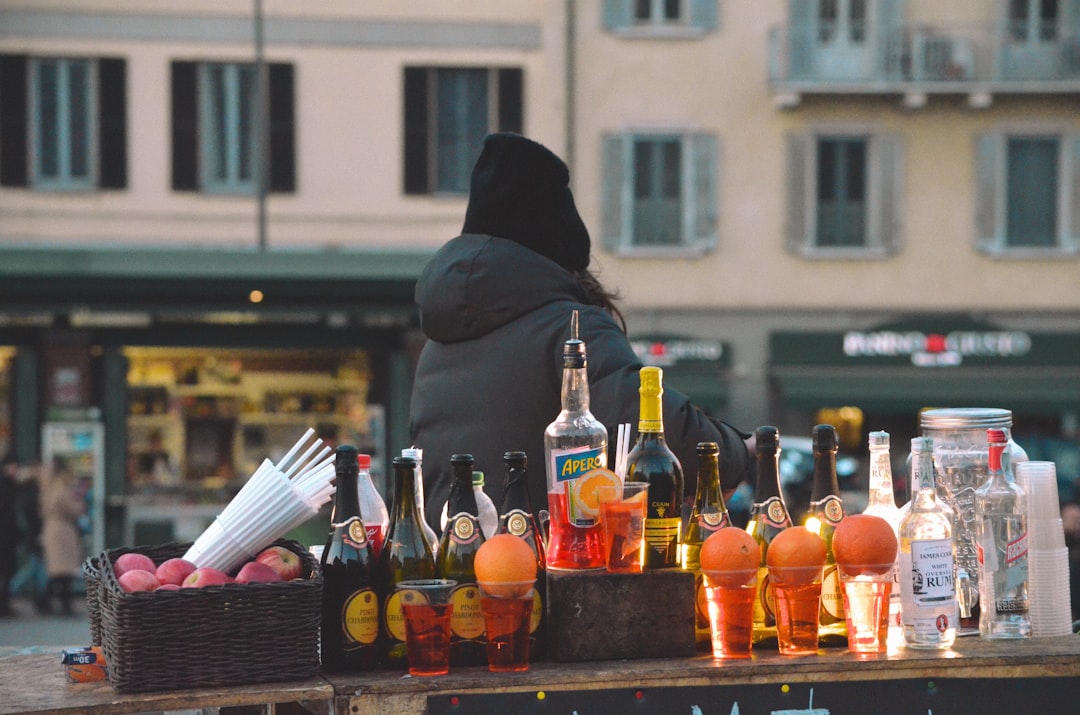 A man tasting fermented drinks at an outdoor market stall lined with probiotic and cultured beverage bottles