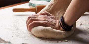 Een bekwame bakker die met de hand een zuurdesembrood vormt, wat het ambacht in de kern van wereldwijde broodtradities weerspiegelt