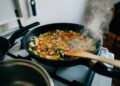 A professional chef making a pan sauce by deglazing a hot skillet with wine in a restaurant kitchen