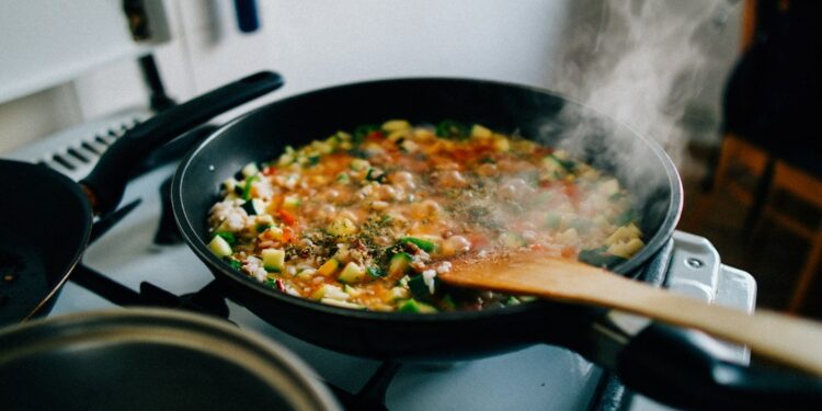 A professional chef making a pan sauce by deglazing a hot skillet with wine in a restaurant kitchen