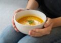 chef-plating-herfstsoep-keuken-unsplash - GUSTOwebzine Een chef-kok dresseert zorgvuldig een kom met herfstgerechten in een professionele keuken, waarmee hij klassieke technieken uit het oogstseizoen demonstreert