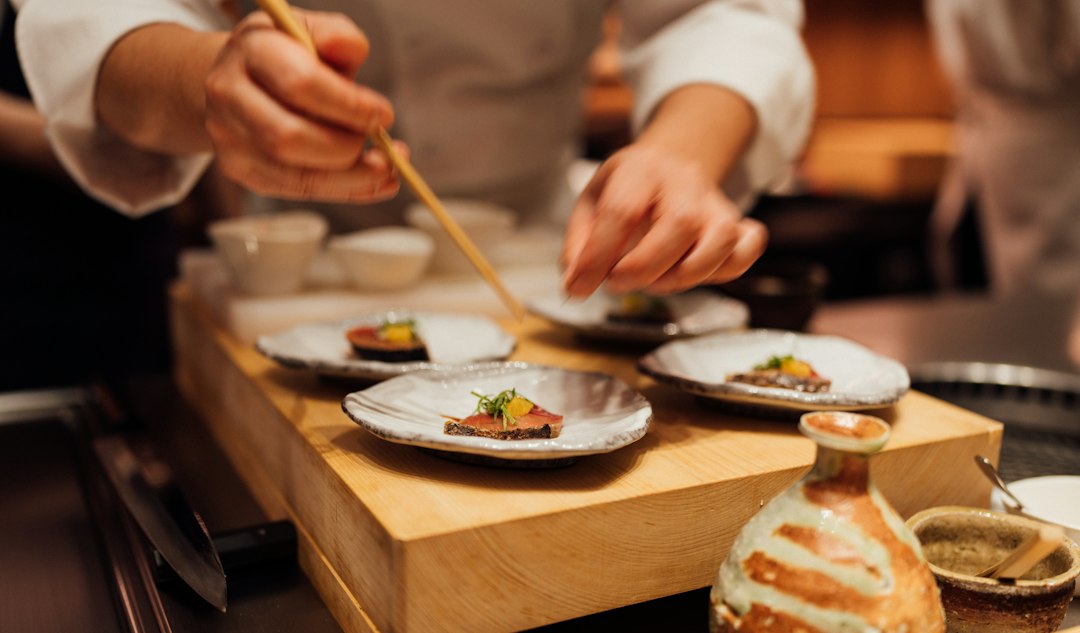 A chef plating a complex umami-rich dish developed using koji fermentation techniques at a modern fine dining restaurant