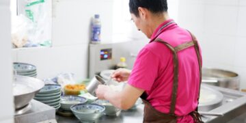 A chef carefully building an aromatic base in a pot, preparing a classic one-pot rice dish with layered spices and stock.