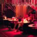 Dineren op een terras in Dubai 6 plekken om nu te reserveren - GUSTOwebzine Groep vrienden gezeten aan ronde buitentafels onder een gestreepte luifel, drankjes en bloemen op tafel in roze avondlicht.