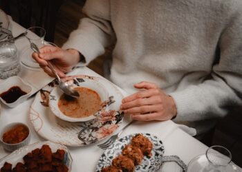Een persoon proeft op smaak met een houten lepel terwijl deze een onbekend wereldgerecht kookt in een restaurantkeuken.