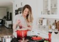 woman-cooking-unsplash - GUSTOwebzine Een kok roert voorzichtig langzaam gegaarde bonen in een aardenwerken pot boven een laag vuur, wat de klassieke techniek illustreert
