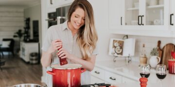 woman-cooking-unsplash - GUSTOwebzine Een kok roert voorzichtig langzaam gegaarde bonen in een aardenwerken pot boven een laag vuur, wat de klassieke techniek illustreert