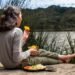 EU regional cheeses at peak in September - GUSTOwebzine Girl sitting barefoot on a wooden dock by a lake, eating orange slices from a metal cup with a plate of food beside her.