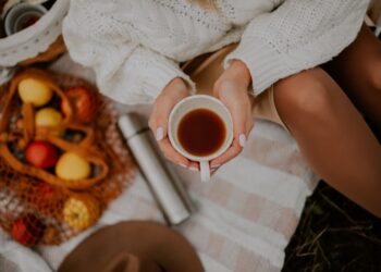 Een vrouw houdt een keramieken mok met warme gekruide dranken vast naast herfstbladeren, wat het seizoensgebonden comfort van dranktradities laat zien.