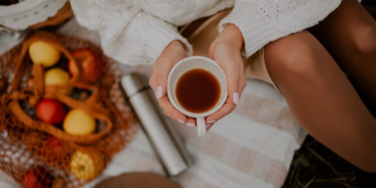 Een vrouw houdt een keramieken mok met warme gekruide dranken vast naast herfstbladeren, wat het seizoensgebonden comfort van dranktradities laat zien.