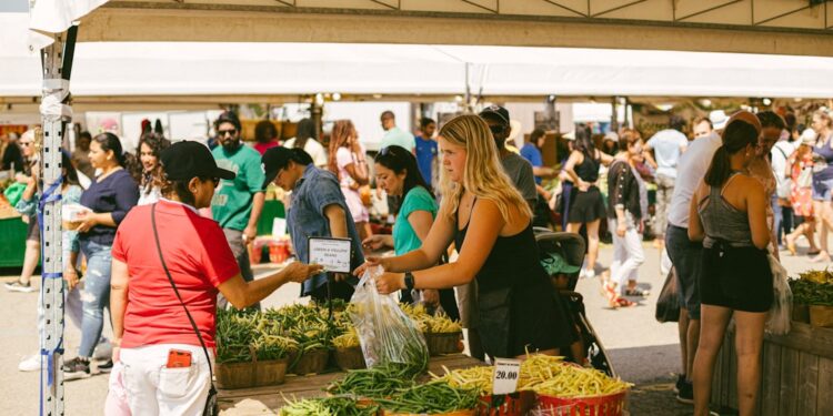 vrouw-shopt-op-boerenmarkt-unsplash - GUSTOwebzine Een vrouw kiest seizoensgroenten op oogstmarkten in Europa tijdens september, met kratten vol verse producten uitgestald.