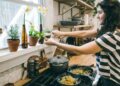 A home cook carefully stirring a warm grain dish in a large pot, surrounded by seasonal root vegetables on a kitchen counter