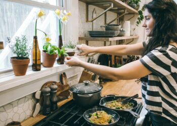 A home cook carefully stirring a warm grain dish in a large pot, surrounded by seasonal root vegetables on a kitchen counter