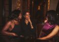 Private dining clubs Londons best rooms - GUSTOwebzine Three women sit together at a dimly lit restaurant table, laughing and chatting warmly while wearing stylish outfits.