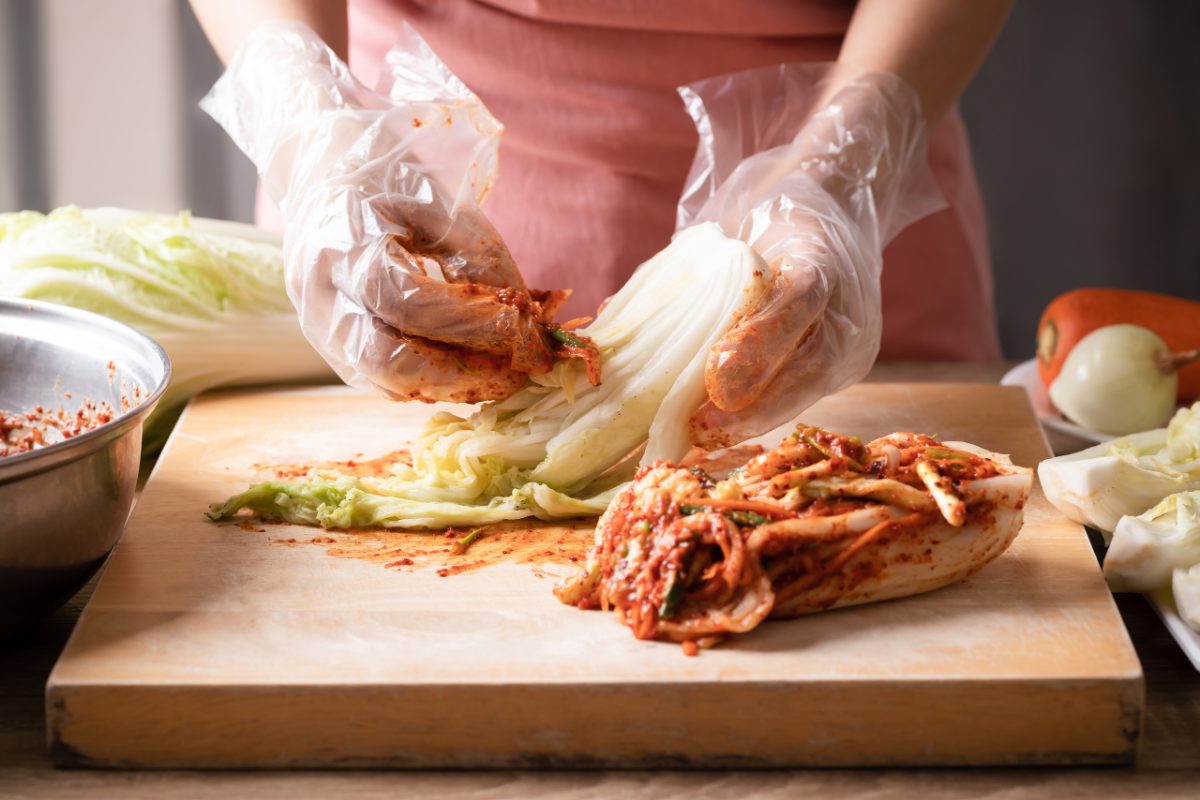 Une femme prépare le kimchi à la main, en superposant le chou dans une jarre traditionnelle, démontrant l'art ancestral derrière ce plat.