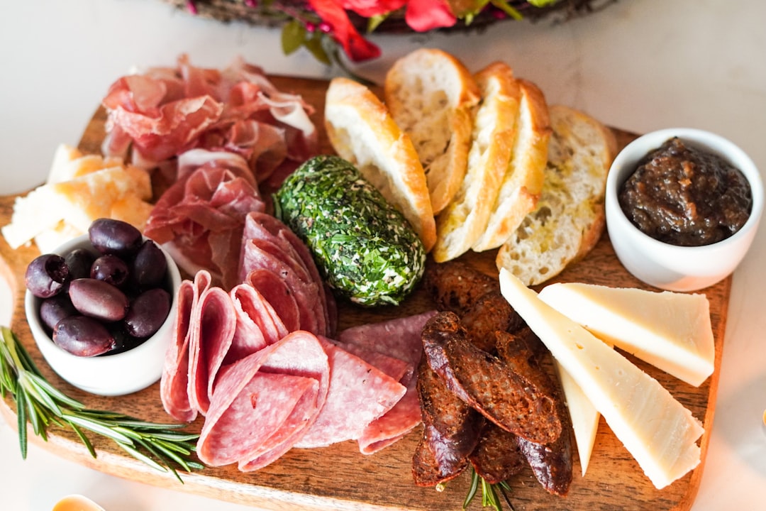 uma tábua de petiscos de verão colorida com itens básicos da despensa global, incluindo carnes curadas, queijo e frutas frescas em uma superfície de madeira