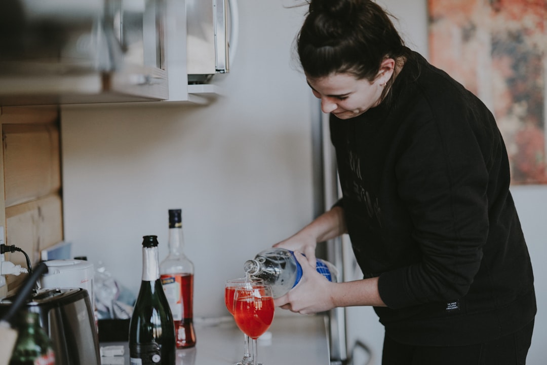 Uma mulher servindo cuidadosamente um copo de bebidas fermentadas em uma bancada de cozinha iluminada, cercada por produtos sazonais de outono