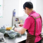 Um chef construindo cuidadosamente uma base aromática em uma panela, preparando um clássico prato de arroz de uma panela só com especiarias em camadas e caldo.