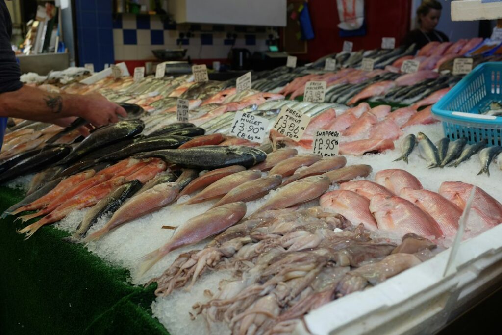 Seafood stall with multiple fish laid on crushed ice and handwritten price signs at a market.